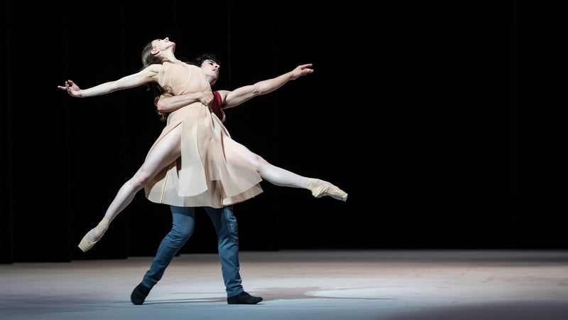 Hamburger Ballet Epilogue - Ballerina, gekleidet in ein helles Akris Kleid scheint über die Bühne zu schweben, gestützt in den Armen eines Ballerino.